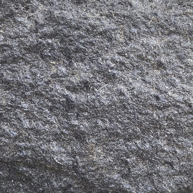 Detailed view of a large black granite rock with a few smaller rocks nearby, highlighting the rugged surface and contrast