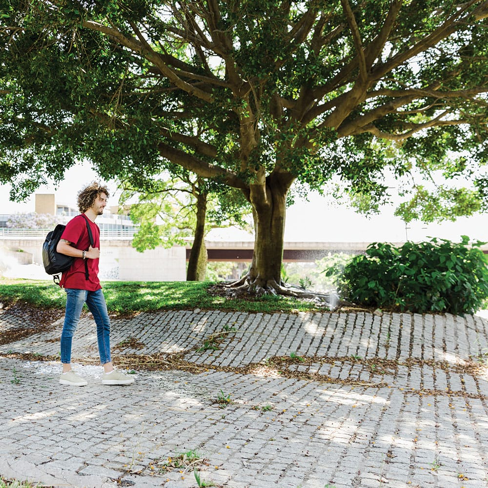 A young man with a backpack strolls along a brick path in a vibrant granite public plaza