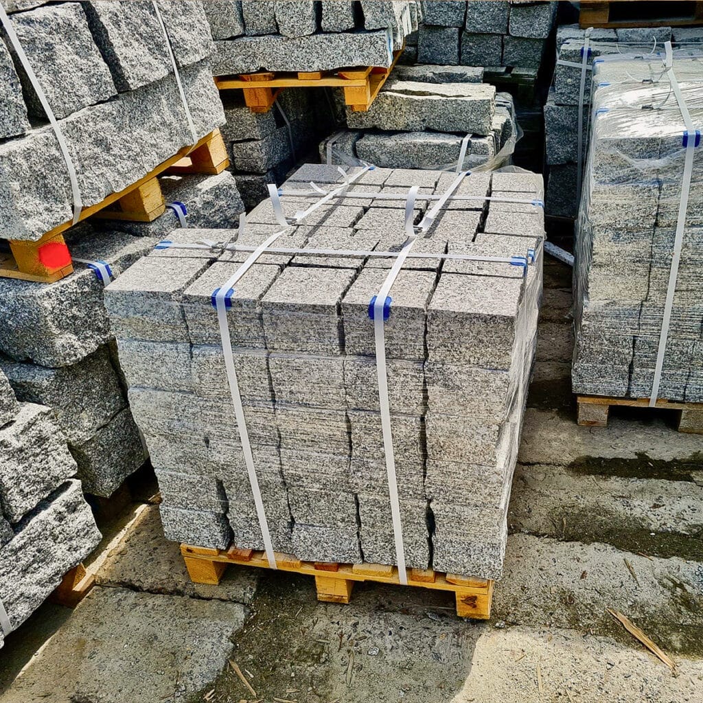 A stack of gray granite blocks arranged on pallets, showcasing the texture and color of granite cobbles