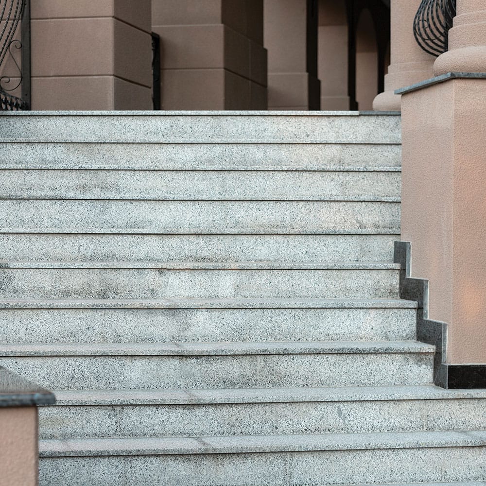 Granite stone steps lead up to a building entrance adorned with columns and decorative railings on the sides