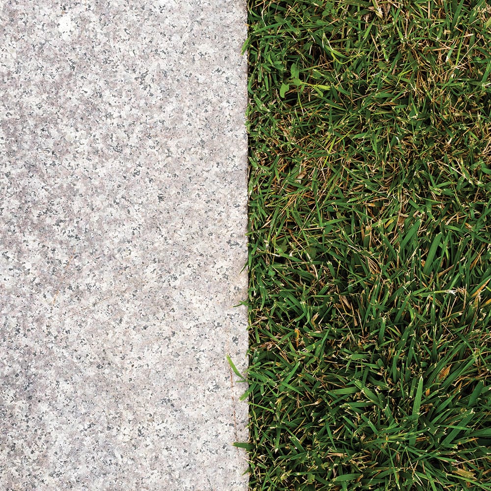 Lush grass bordered by granite slabs, with a concrete sidewalk enhancing the natural landscape of the area