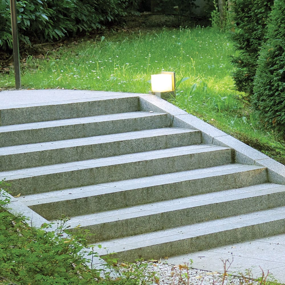 A concrete stairway with granite steps, surrounded by lush greenery in a serene garden setting