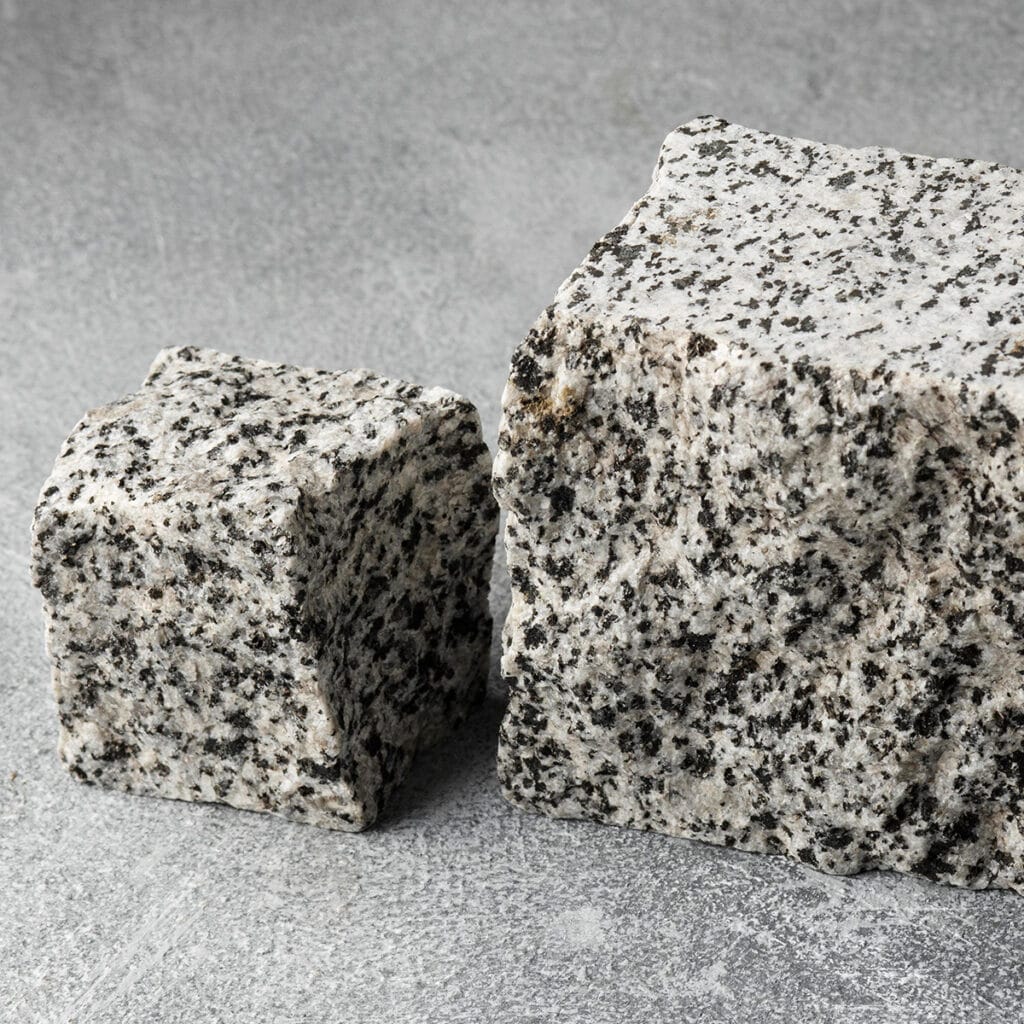 Two blocks of gray granite resting on a textured gray surface, showcasing their natural stone features.