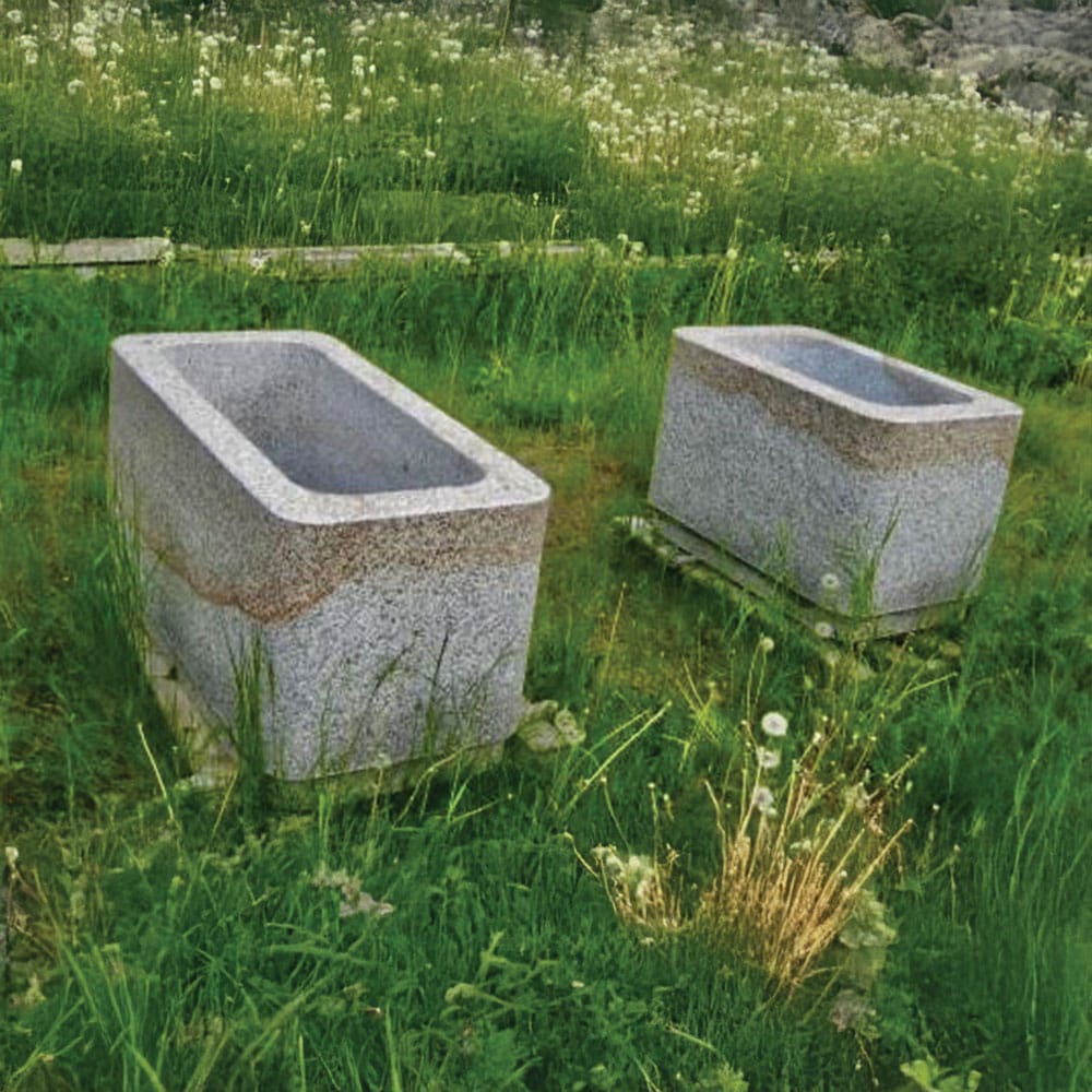 Two granite planters placed in lush green grass, enhancing the garden's aesthetic appeal.