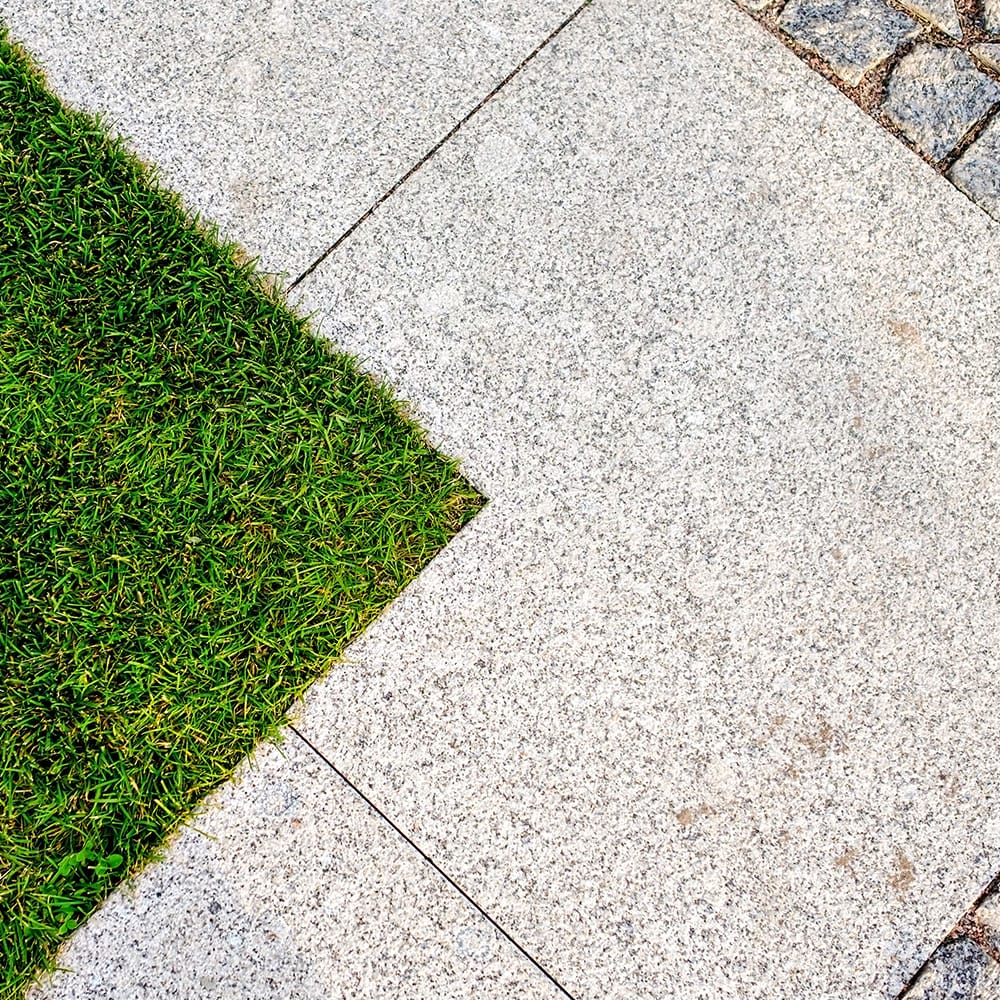 A grassy area featuring a stone walkway made of granite tiles and slabs, surrounded by a lush green lawn