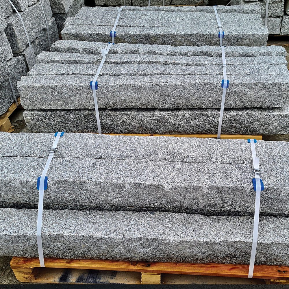 Large gray granite blocks arranged on pallets, illustrating granite palisades prepared for architectural applications