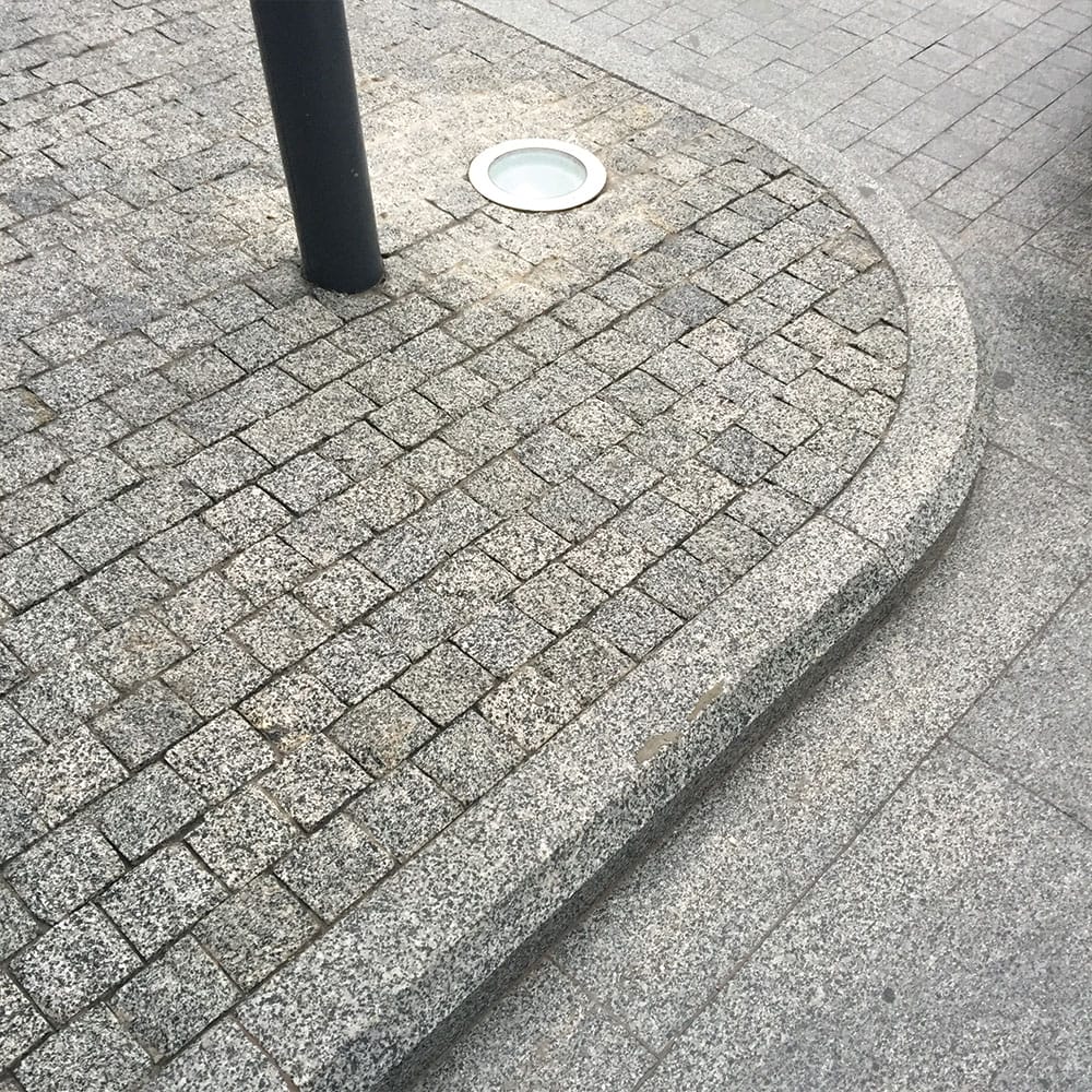 A black light rests on the ground adjacent to a brick sidewalk, bordered by granite curbs