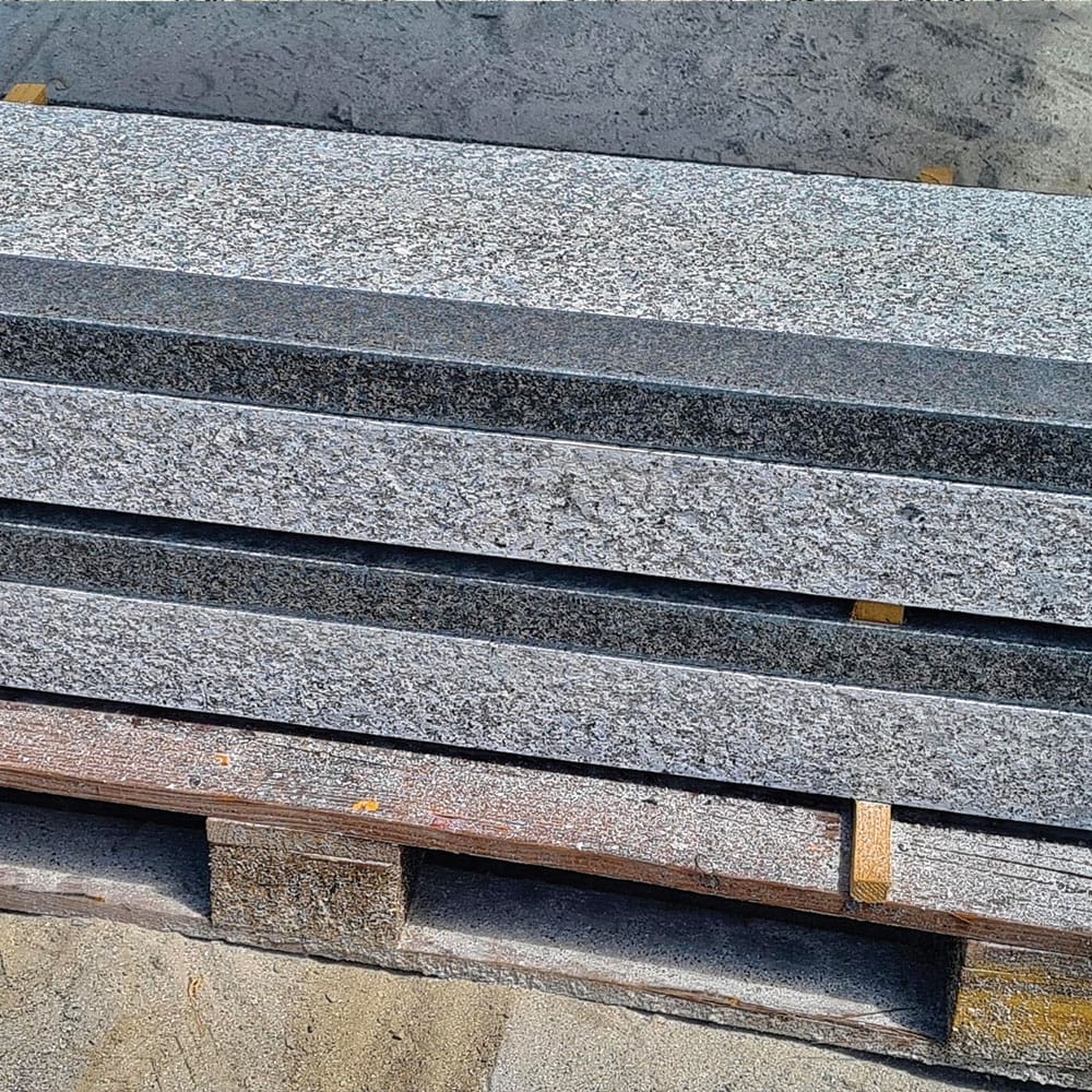 A pallet stacked with grey and black granite steps, ready for installation in exterior, showcasing their textured surface