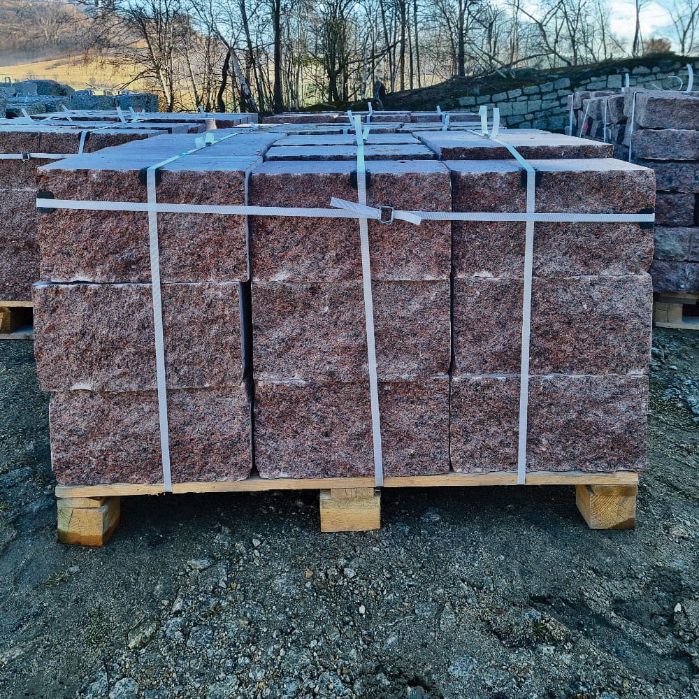 A stack of red granite blocks on pallets, showcasing vibrant vanga color, prepared for transport